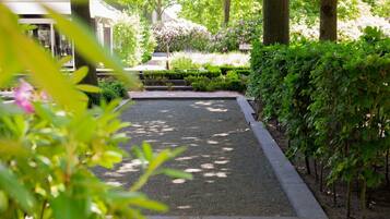 Een tuin met een grindpad, keurig bijgesnoeide heggen en verschillende bloeiende planten.