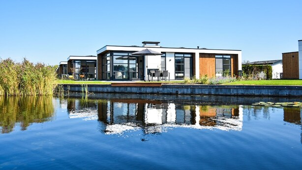 Une maison moderne avec une façade en verre, une terrasse en bois et un bassin devant.