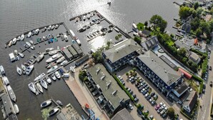 Vue aérienne d’une marina avec des bateaux amarrés, un parking et des bâtiments adjacents.
