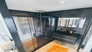Casa de banho moderna com cabine de duche em vidro, toucador escuro com espelho e um tapete de madeira.