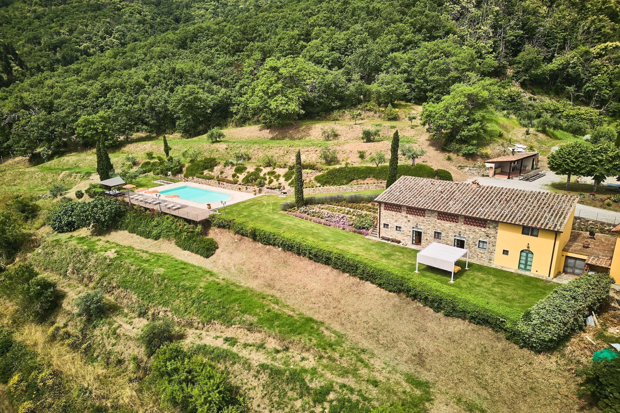 An aerial view of a property with a swimming pool, a well-maintained lawn, and a building with a tiled roof.