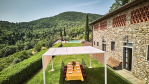 An outdoor dining area with a table set for six, surrounded by stone walls and a view of a mountain. - Farmhouse in Chianti with Pool and Garden (Cavriglia)