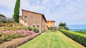 A stone building with a stone facade and a yellow roof, surrounded by well-maintained gardens and a clear view of the mountains. - Farmhouse in Chianti with Pool and Garden (Cavriglia)
