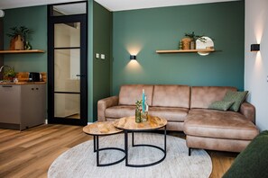 Uma sala de estar moderna com um sofá de couro marrom, duas mesinhas de centro redondas e piso de madeira.