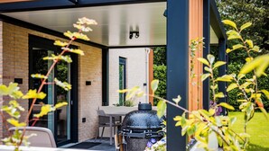 An outdoor patio area with a grill, a table, and chairs. - Holiday Home in Veluwe near Nature Park (Voorthuizen)