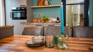 A modern kitchen with a dining table, a teal candle, and decorative glassware. - Holiday Home in Veluwe near Nature Park (Voorthuizen)