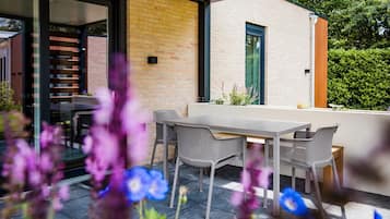 Une terrasse extérieure avec une table et des chaises, une porte vitrée donnant sur un escalier et un mur en briques.
