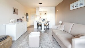 Una sala de estar moderna con un sofá, una mesa de comedor con sillas, una zona de cocina con armarios y una pequeña estatua decorativa sobre la encimera.