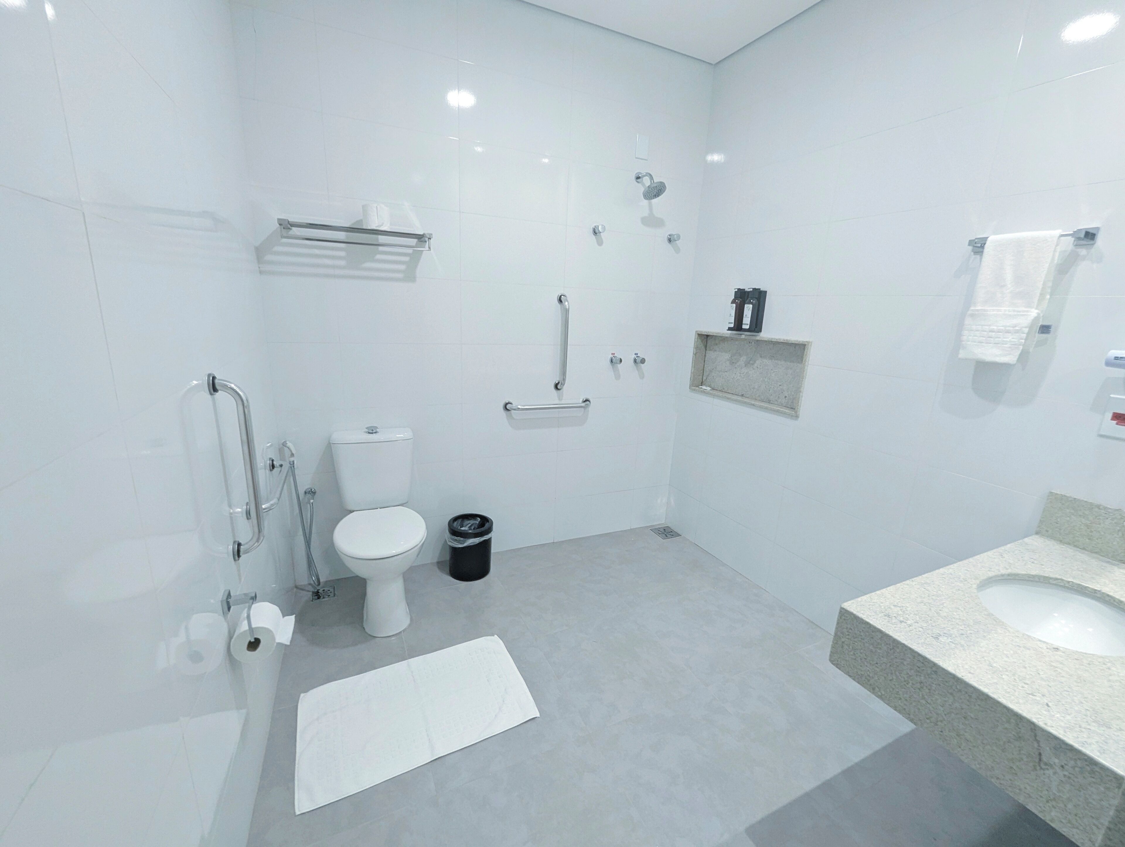 A modern bathroom with a toilet, bidet, handrail, and a sink.