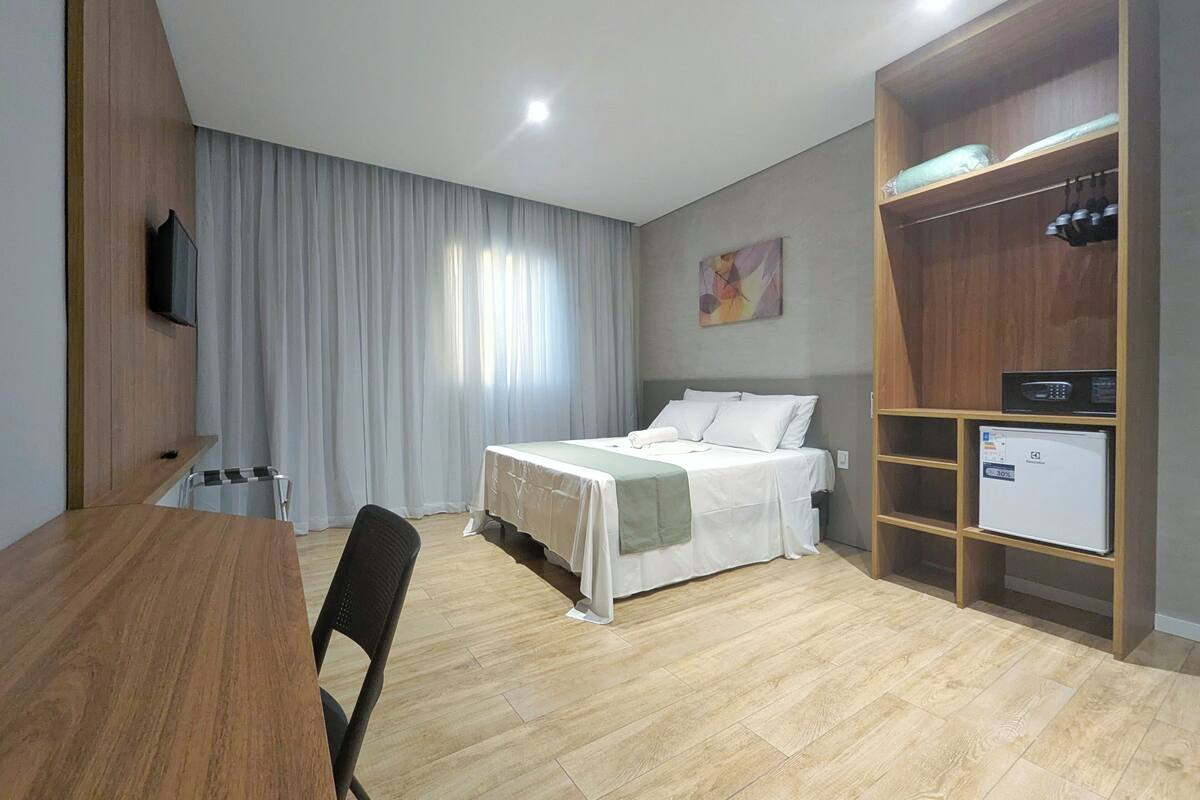 A hotel room with a bed, a desk, a chair, a wardrobe, and a television.