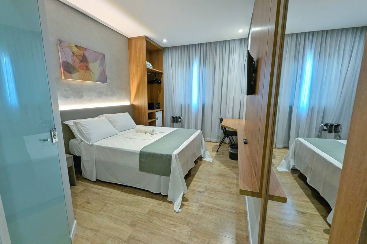 A hotel room with a bed, a desk, a chair, a wardrobe, and a TV.