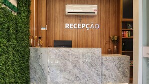 Een receptiebalie met een marmeren aanrecht, een televisie en een bordje met de tekst 'RECEPCAO'.