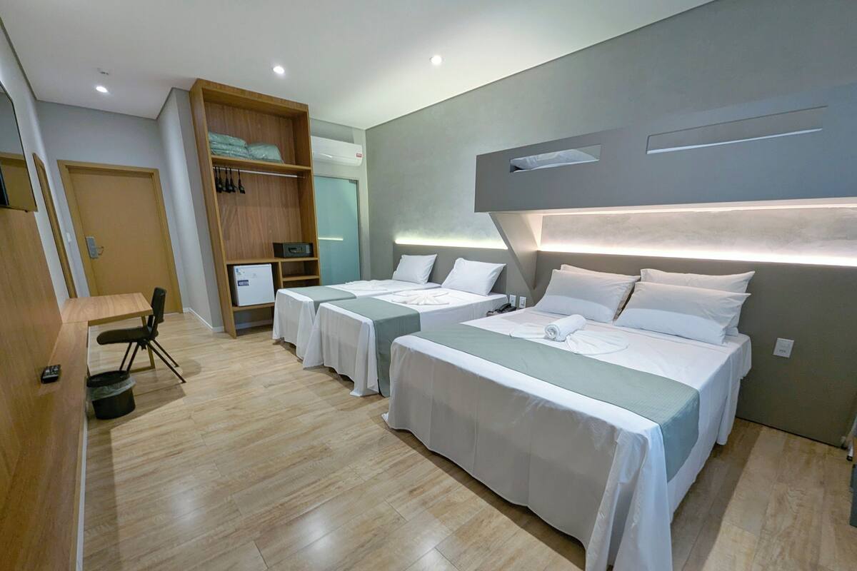A hotel room with two beds, a desk, a chair, a wardrobe, and a small kitchenette.