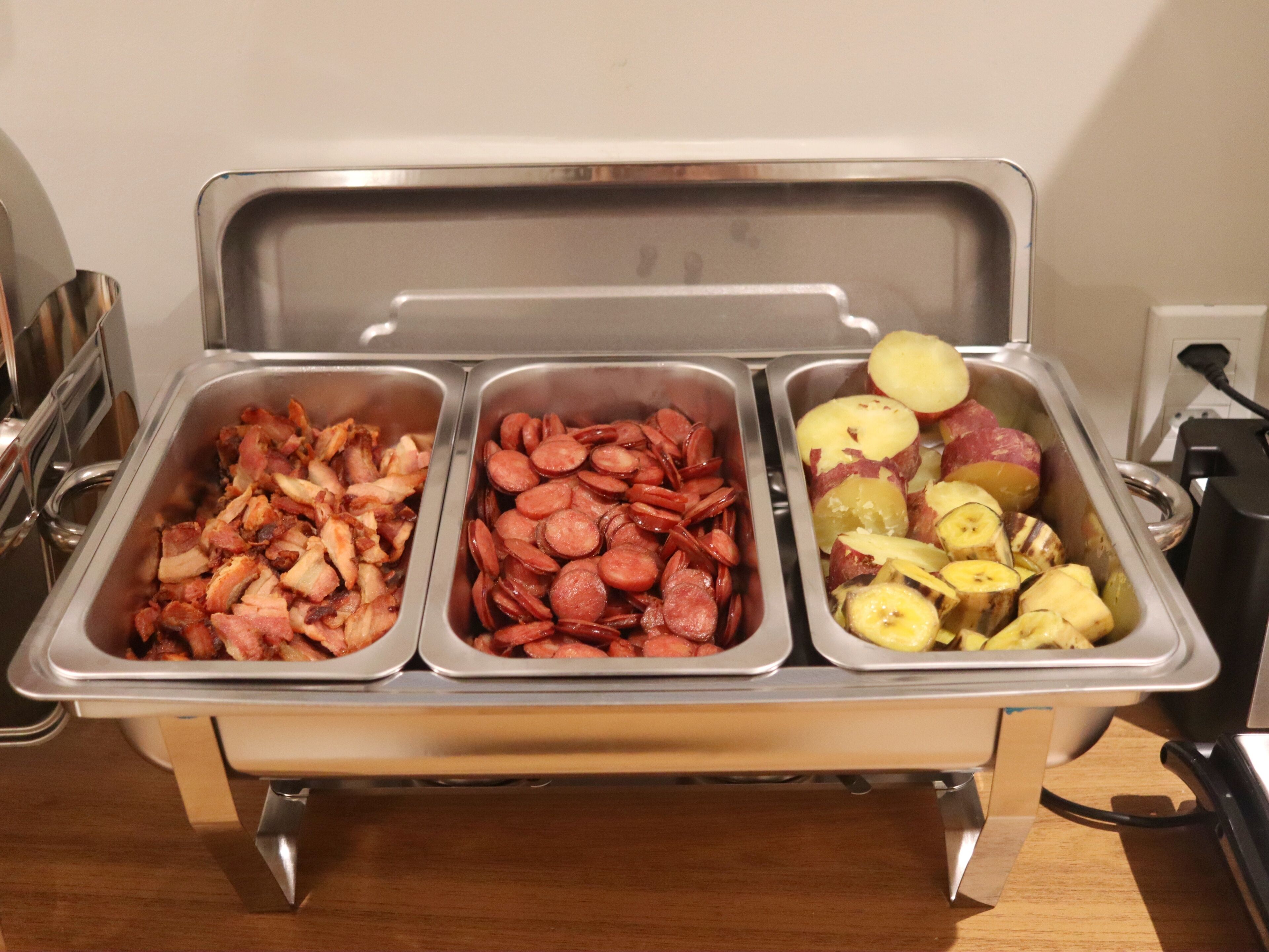 Un bufé con tres fuentes de comida: tocino, salchicha y papas.