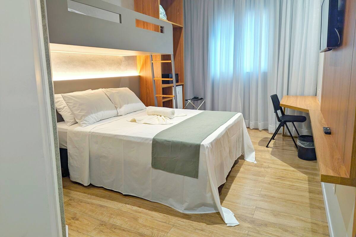 A hotel room with a bed, a desk, a chair, and a TV mounted on the wall.