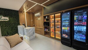 Een hotel receptie met een receptiebalie, een zithoek met een bank en een drankkoelkast gevuld met diverse dranken.