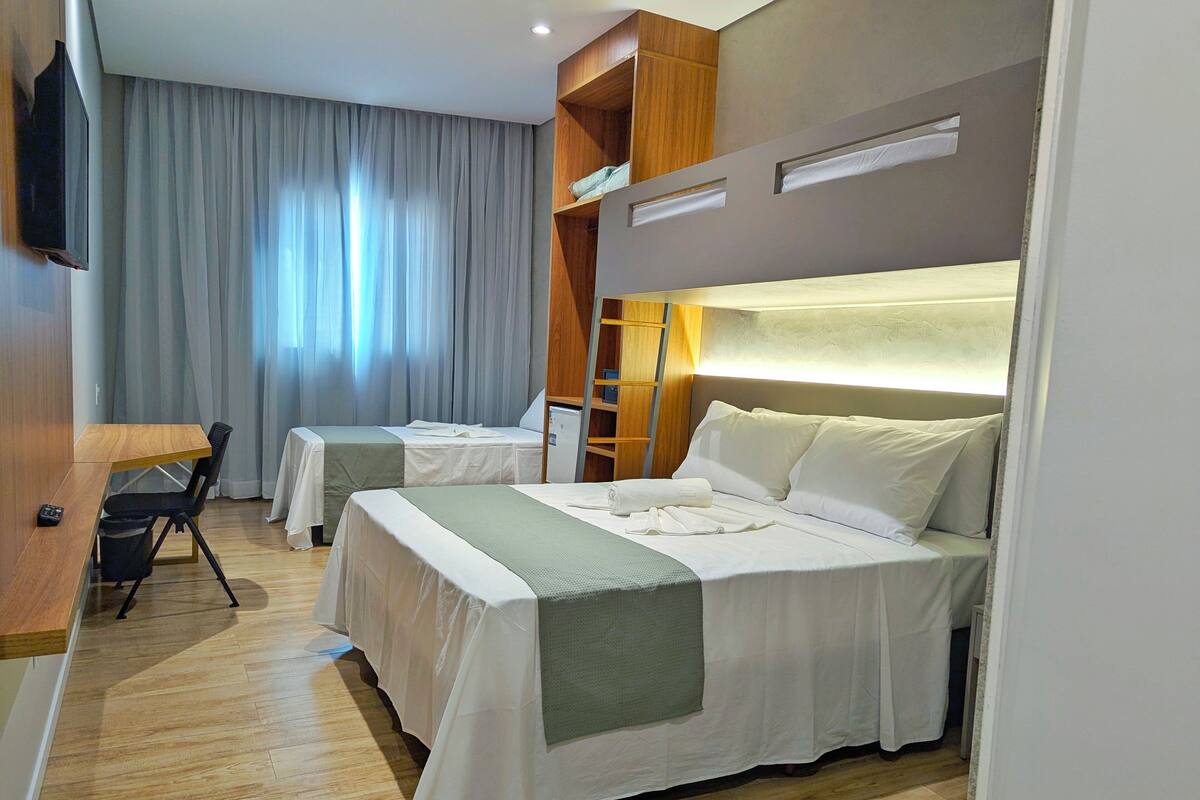 A hotel room with two beds, a desk, a chair, and a TV.