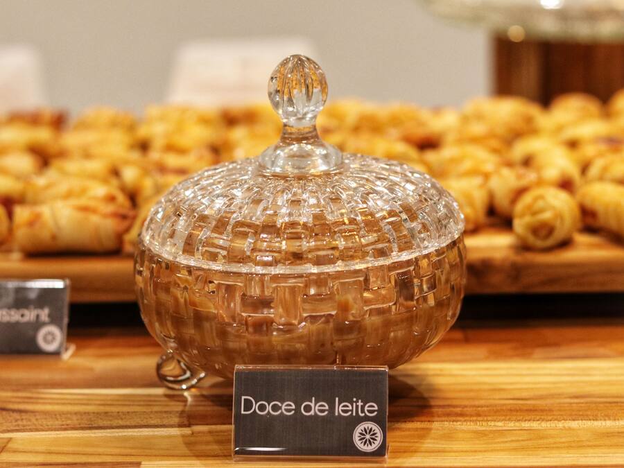 En glasburk märkt med texten ”Doce de leite” står på en träyta, med bakverk i bakgrunden.