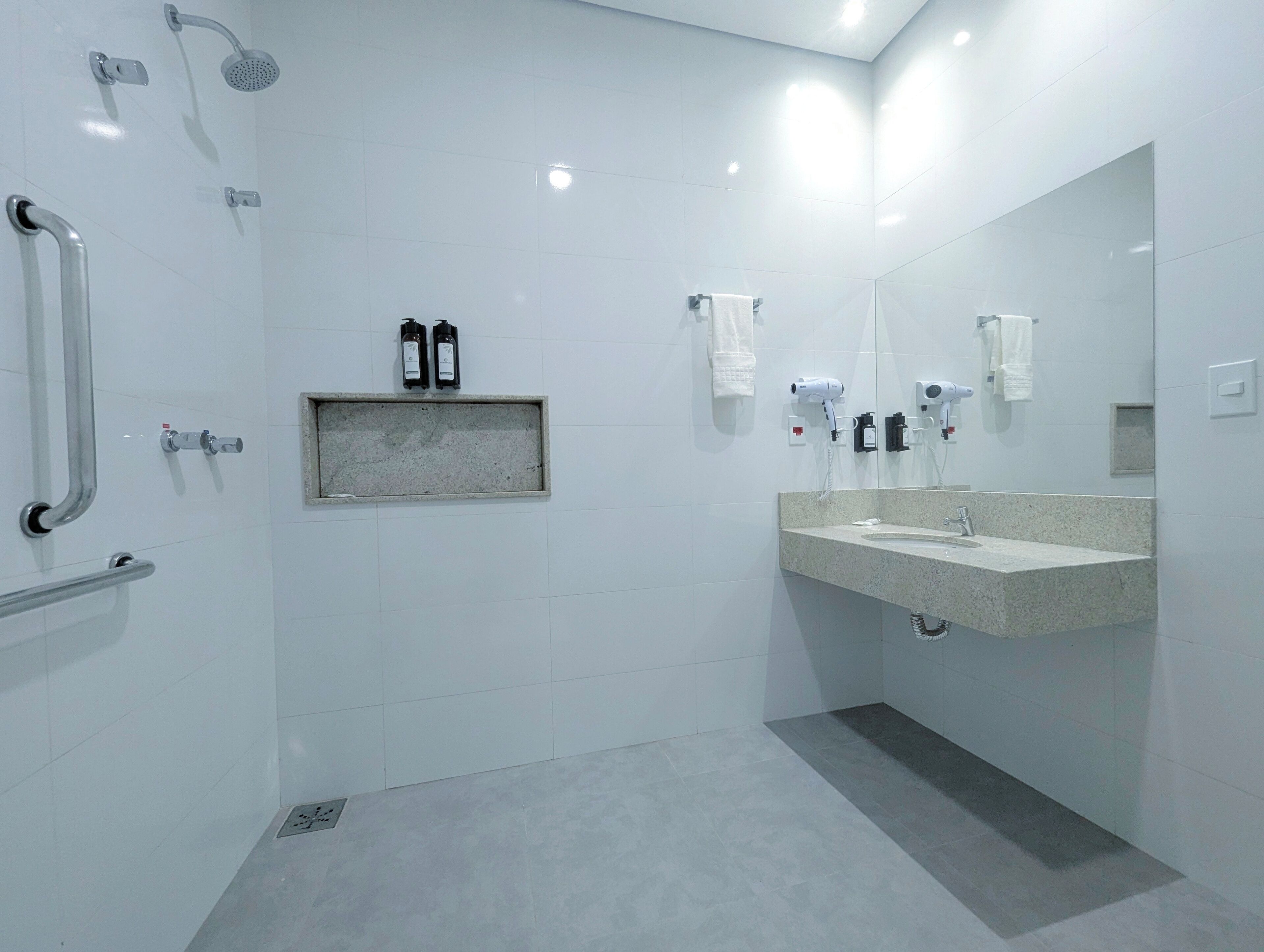 A modern bathroom with a large mirror, a sink, a shower with a handheld showerhead, and a grab bar.