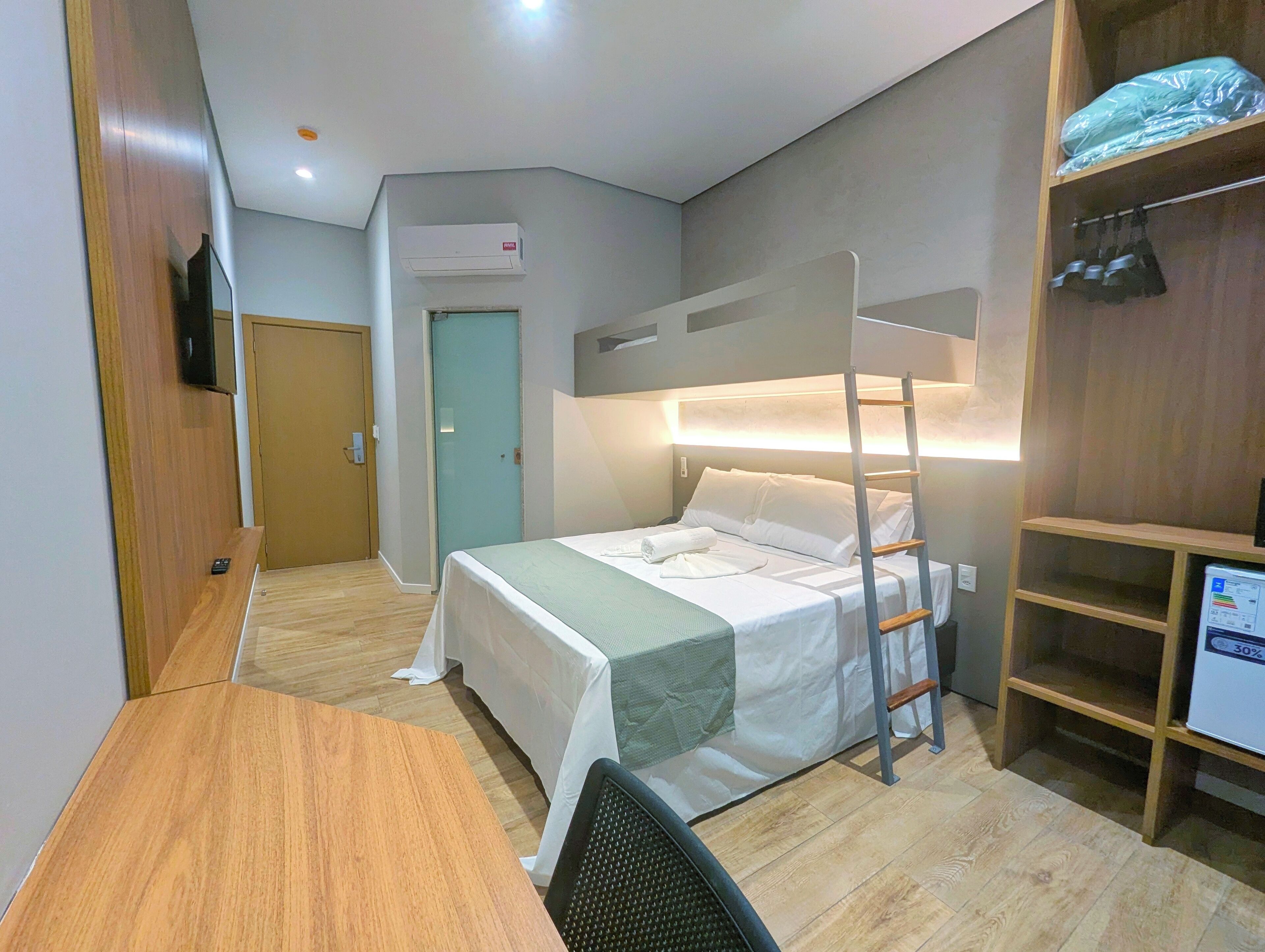 Una habitación de hotel compacta con literas, un escritorio, una silla, un armario y un televisor.