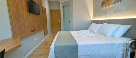 A hotel room with a bed, a TV mounted on the wall, a wooden panel, a door, and a painting on the wall.