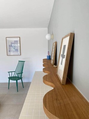 Un intérieur moderne avec une console en bois, un fauteuil vert et des œuvres d’art encadrées accrochées au mur.