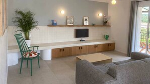 Un salon moderne avec un téléviseur à écran plat, un fauteuil vert, un canapé et une plante en pot.