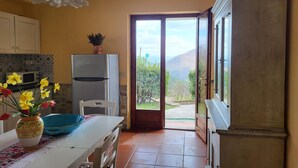 Una cocina con refrigerador, una mesa de comedor con un florero y vista a un paisaje montañoso a través de una puerta de vidrio.