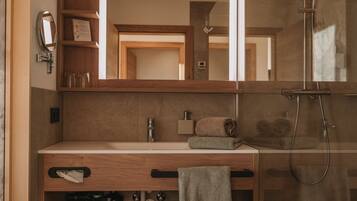 A modern bathroom with a wooden vanity, a large mirror, a shower, and a trash can.