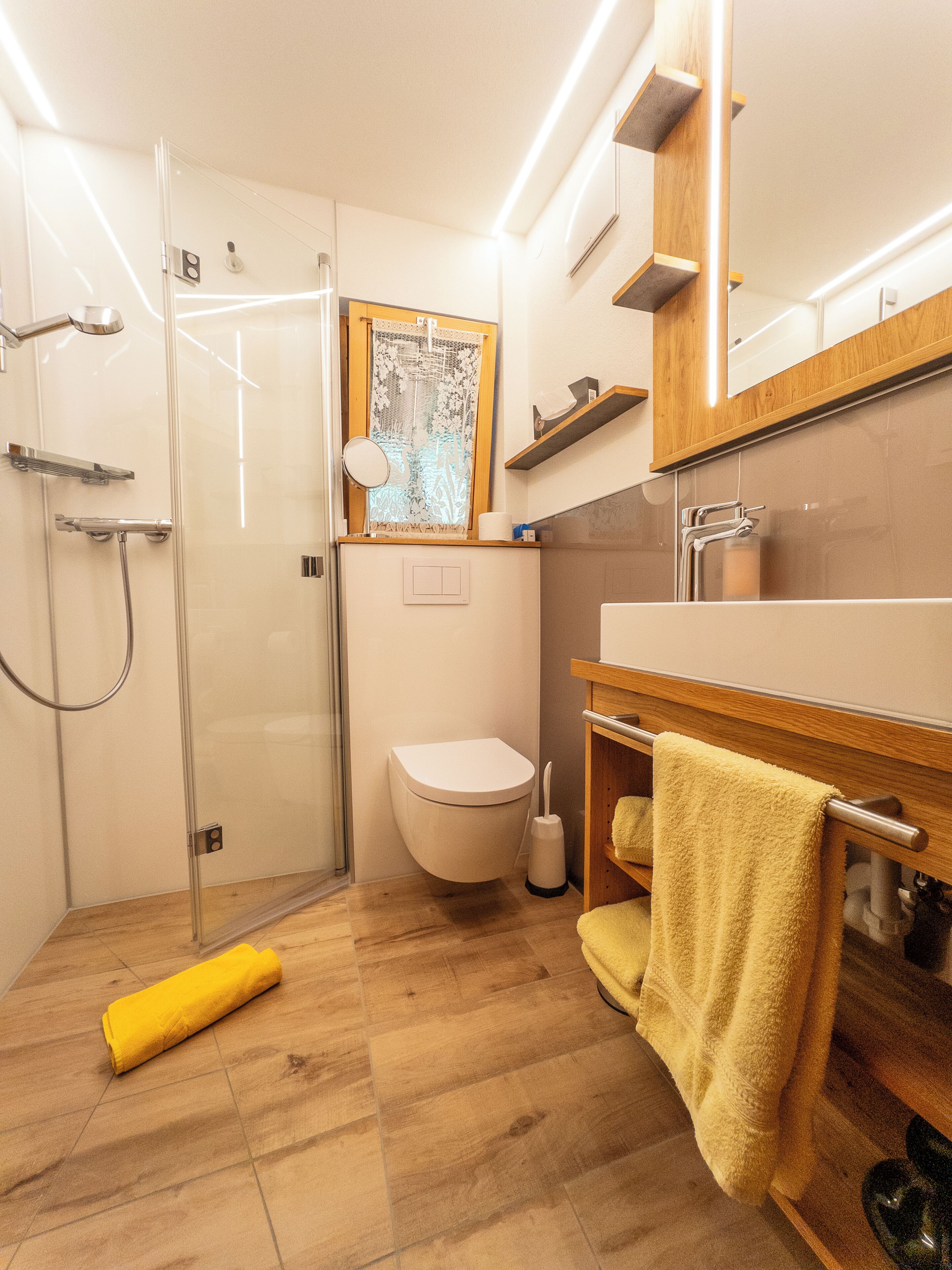 Un baño moderno con cabina de ducha de vidrio, inodoro, lavabo con espejo y suelo de madera.