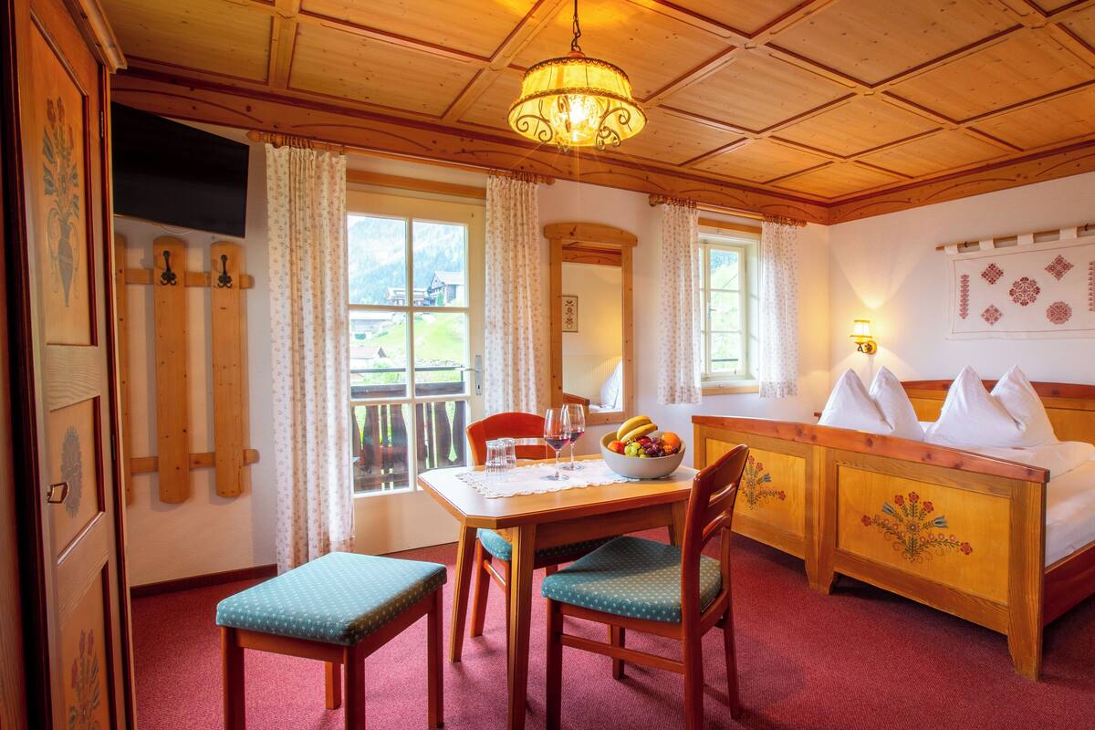 Une chambre d’hôtel avec un plafond en bois, un lit avec des oreillers blancs, une table à manger avec des chaises et un panier de fruits.
