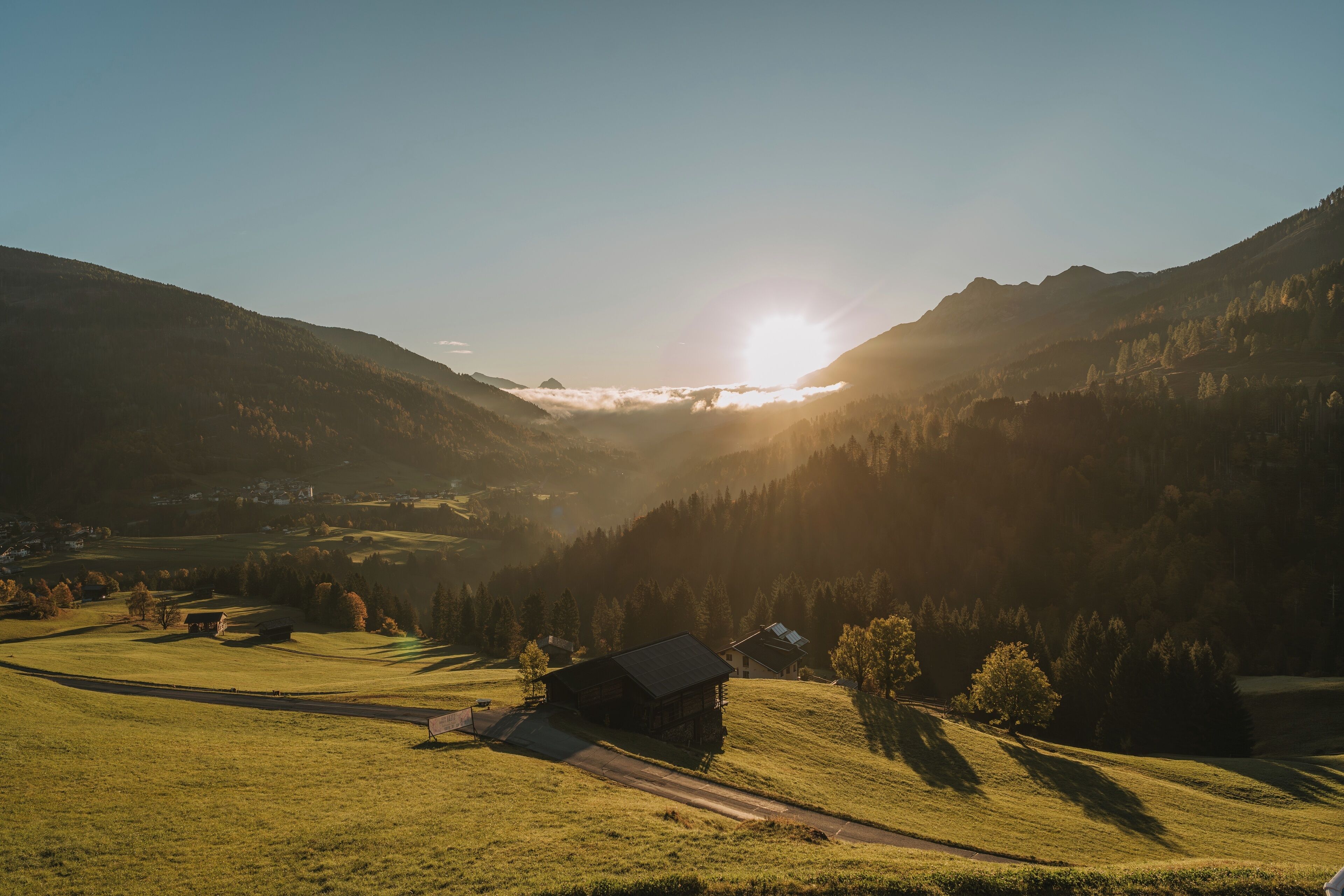 A rural landscape with a small cabin, a road, and surrounding hills.