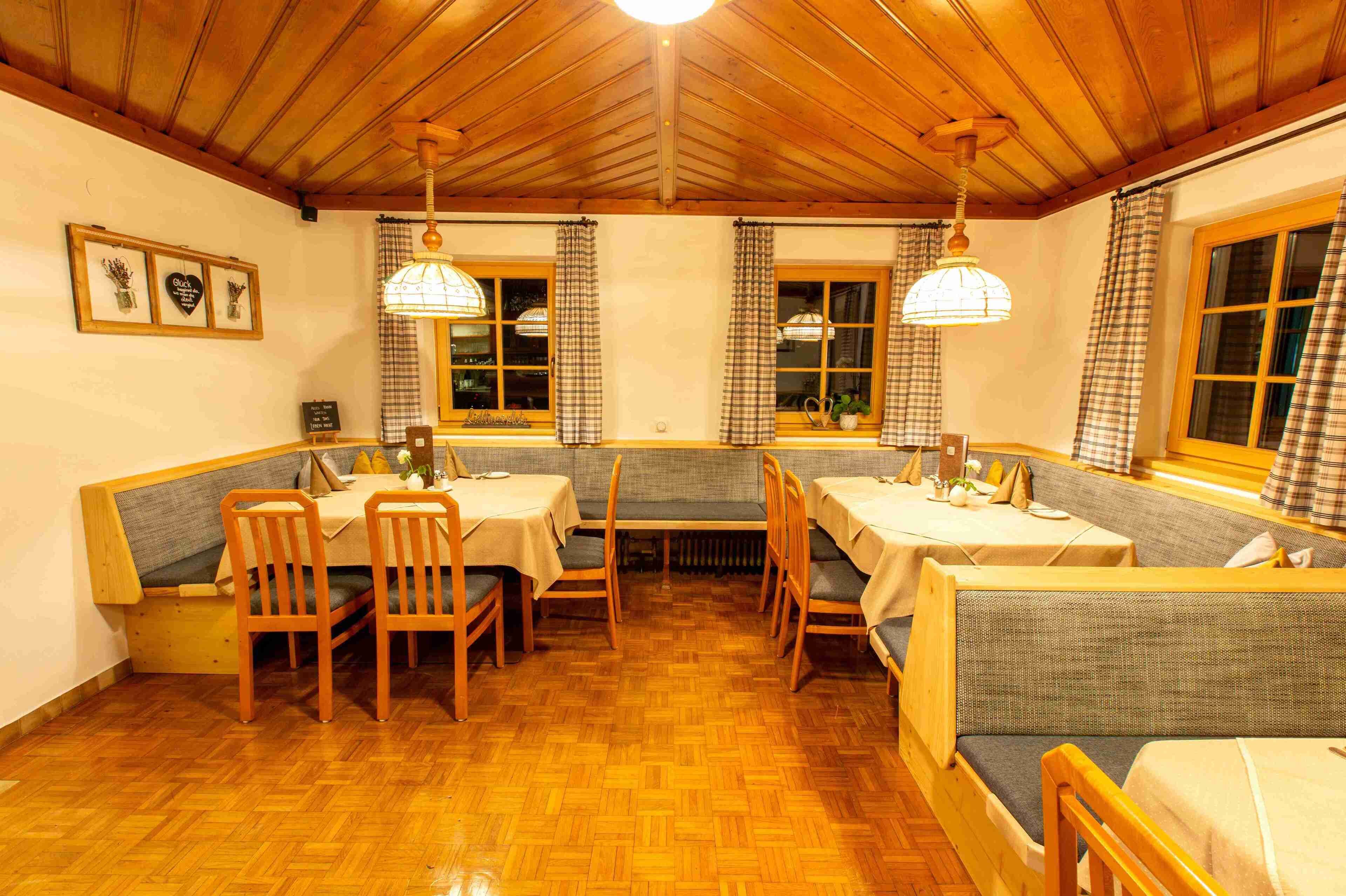 Un rincón comedor acogedor con mesas y bancos de madera, cortinas a cuadros y lámparas colgantes.