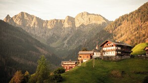 Paisaje de montaña con una edificación de estilo chalet, con balcón y la aguja de una iglesia.