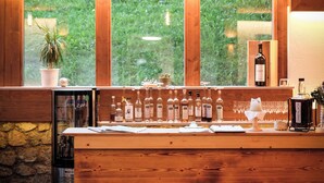 Una zona de bar con barra de madera, un ventanal grande, una lámpara colgante y una botella de vino en la encimera.