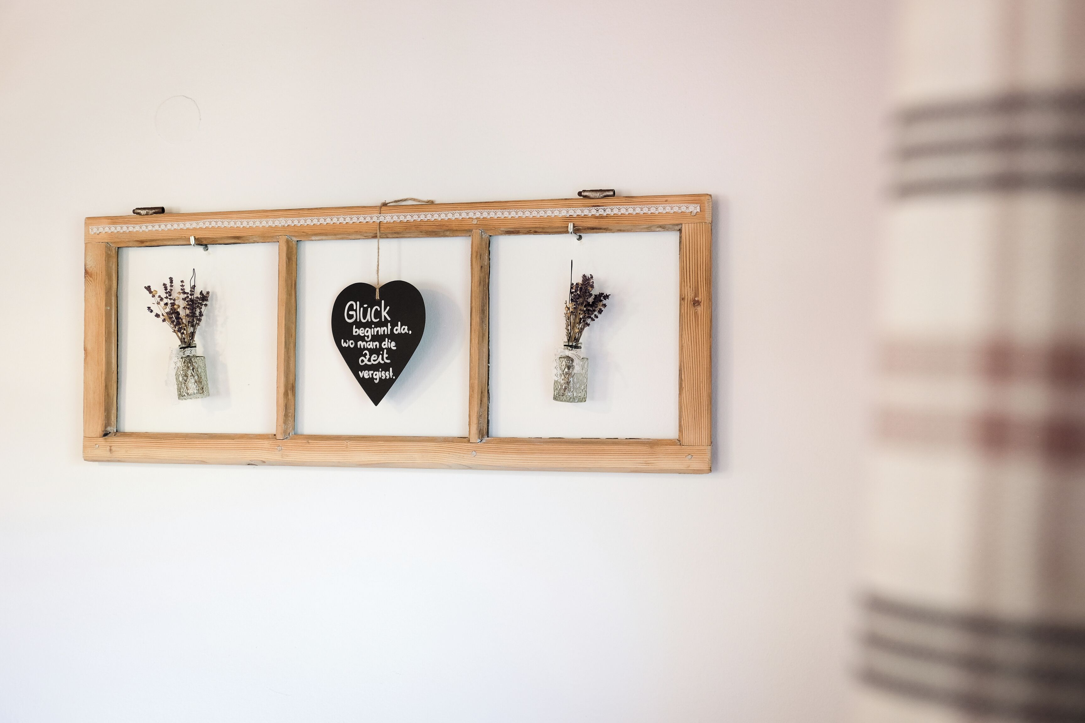 A framed wall decoration with three sections, including a central heart-shaped sign with text and two vases with dried flowers.