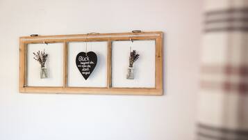 A framed wall decoration with three sections, including a central heart-shaped sign with text and two vases with dried flowers.