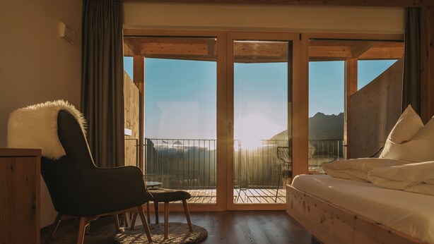 Una habitación con cama, una silla y vistas a montañas a través de amplios ventanales.