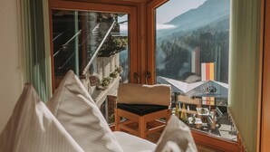 Una habitación acogedora con techo de madera, una cama con ropa blanca, una silla y un ventanal con vistas a la montaña.