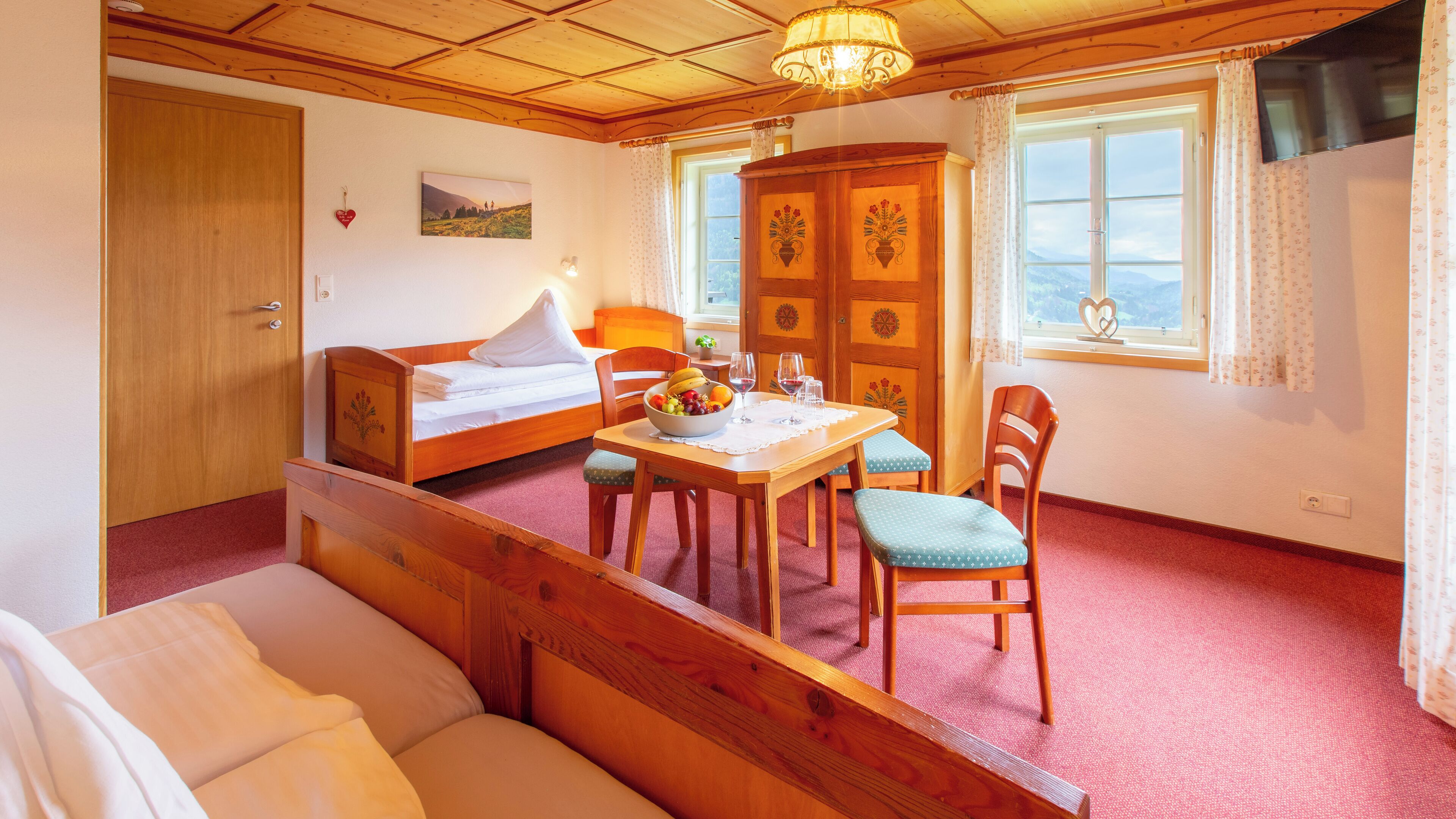 Una habitación acogedora con una cama de madera, una mesa de comedor con sillas, un mueble pequeño y un ventanal con cortinas.