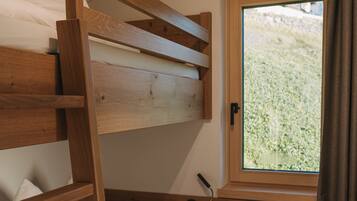 Un letto a castello con struttura in legno, una finestra con vista su del verde e una piccola scrivania di legno con una rivista.