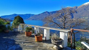A balcony with potted plants and a view of mountains and a lake. - Apartment by Lake Maggiore with Mountain Views (Pino sulla Sponda del Lago Maggiore)