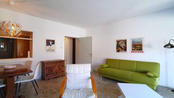 Ein modernes Wohnzimmer mit einem grünen Sofa, einem weißen Sessel, einem Esstisch und einem Holzschrank.