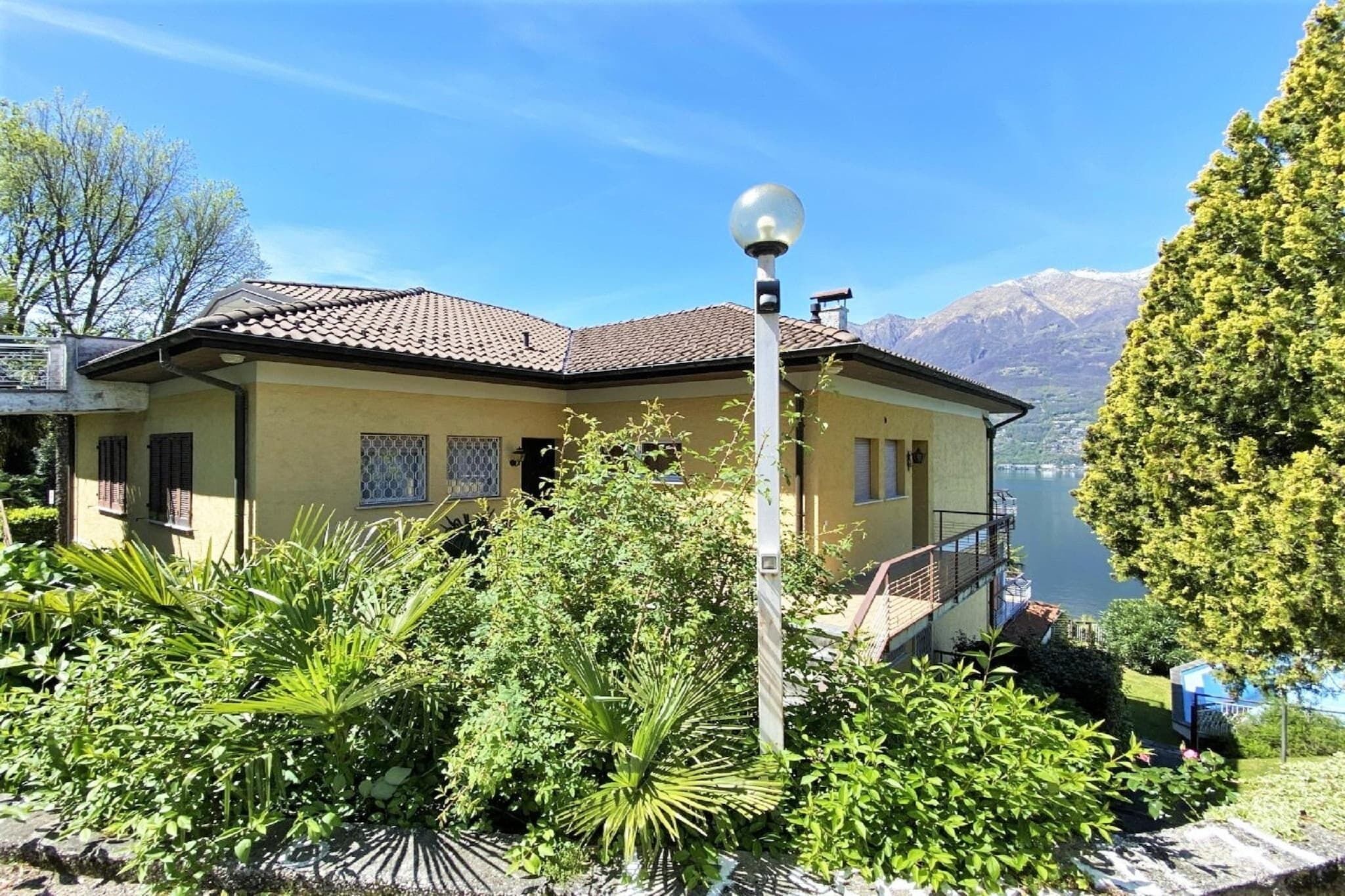 Une maison dotée d’un balcon donnant sur un lac, entourée d’une végétation luxuriante et avec des montagnes en toile de fond.