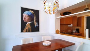 A dining area with a wooden table, white chairs, a painting of a woman, and a kitchen with wooden cabinets and a modern pendant light. - Apartment by Lake Maggiore with Mountain Views (Pino sulla Sponda del Lago Maggiore)