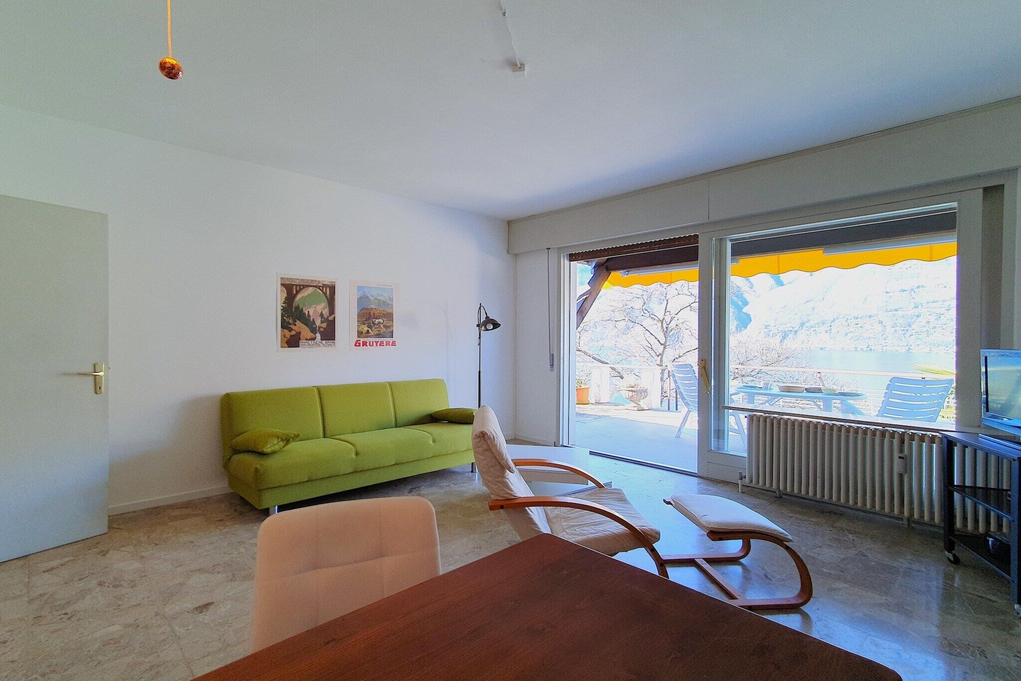 Ein modernes Wohnzimmer mit einem grünen Sofa, einem Holzesstisch und einem großen Fenster mit Blick ins Freie.