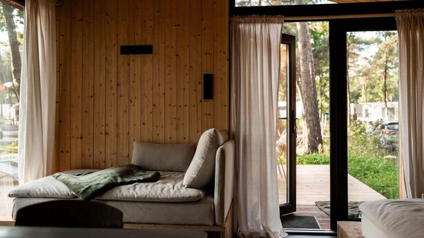 A cozy room with a wooden wall, a bed, and a view of the outdoors.