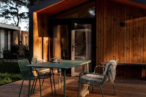 Un patio exterior con cubierta de madera, una mesa con sillas y un ventanal de vidrio que da a un área techada.