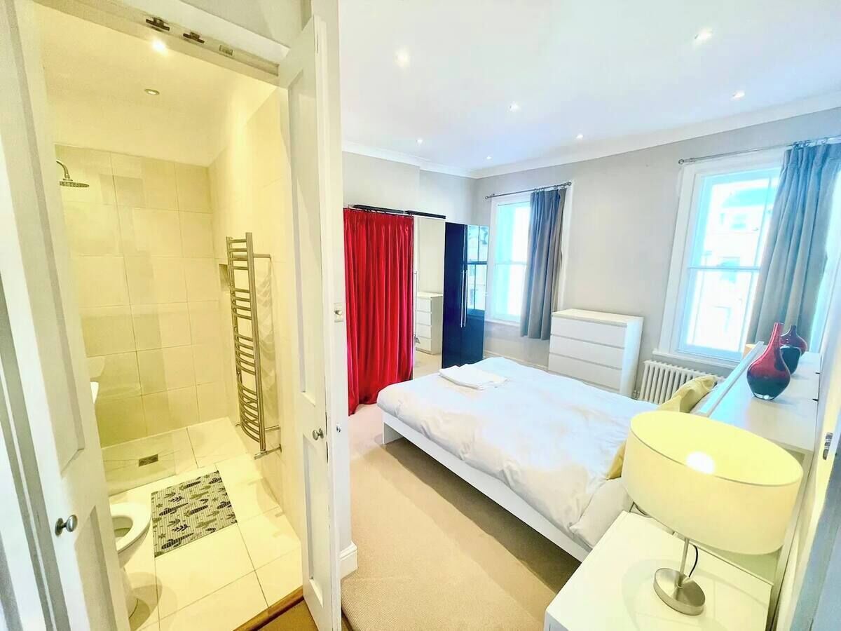 Habitación de hotel con ducha, cama, mesita de noche con lámpara y ventana con cortinas.