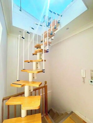 Uma escadaria em espiral com degraus de madeira e guarda-corpos brancos, que dá acesso a um claraboia.